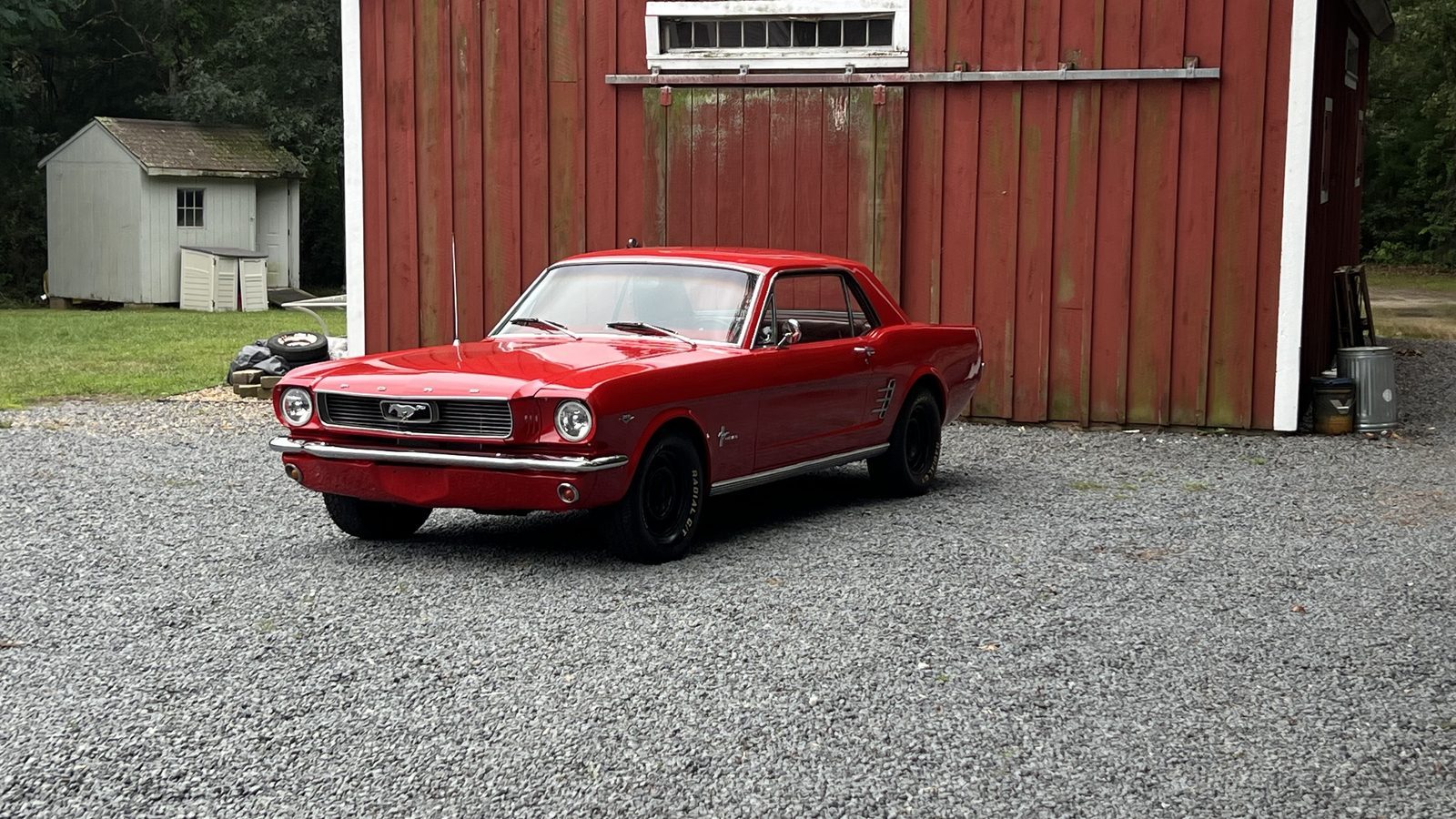 Red 1966 Ford Mustang parked in front of a red barn